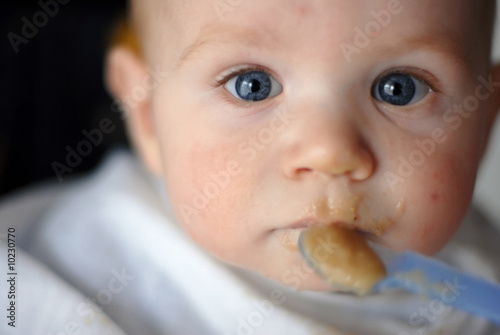 Adorable baby boy having a meal with blue plastic spoon