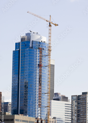 A yellow construction crane erecting a high rise blue glass