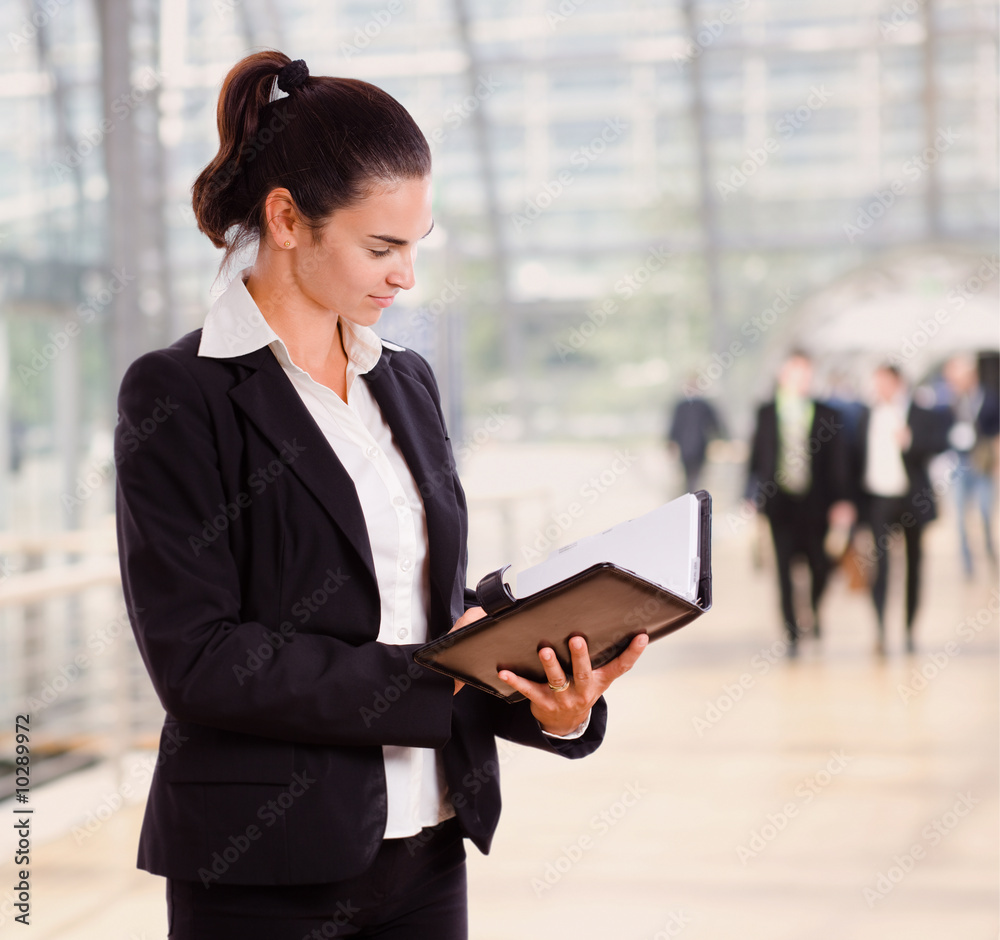 Attractive businesswoman looking at day planner in office lobby. Attractive businesswoman looking at day planner in office lobby.