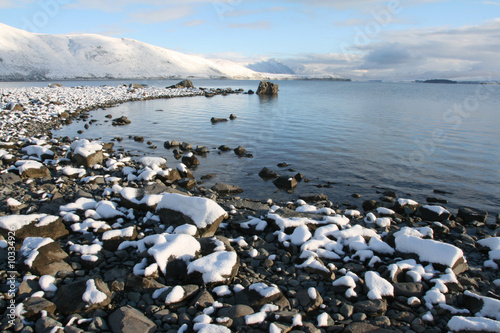Looking across a lake with freshly fallen snow on the stones