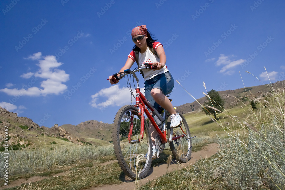 Girl rides a bike in mountains.