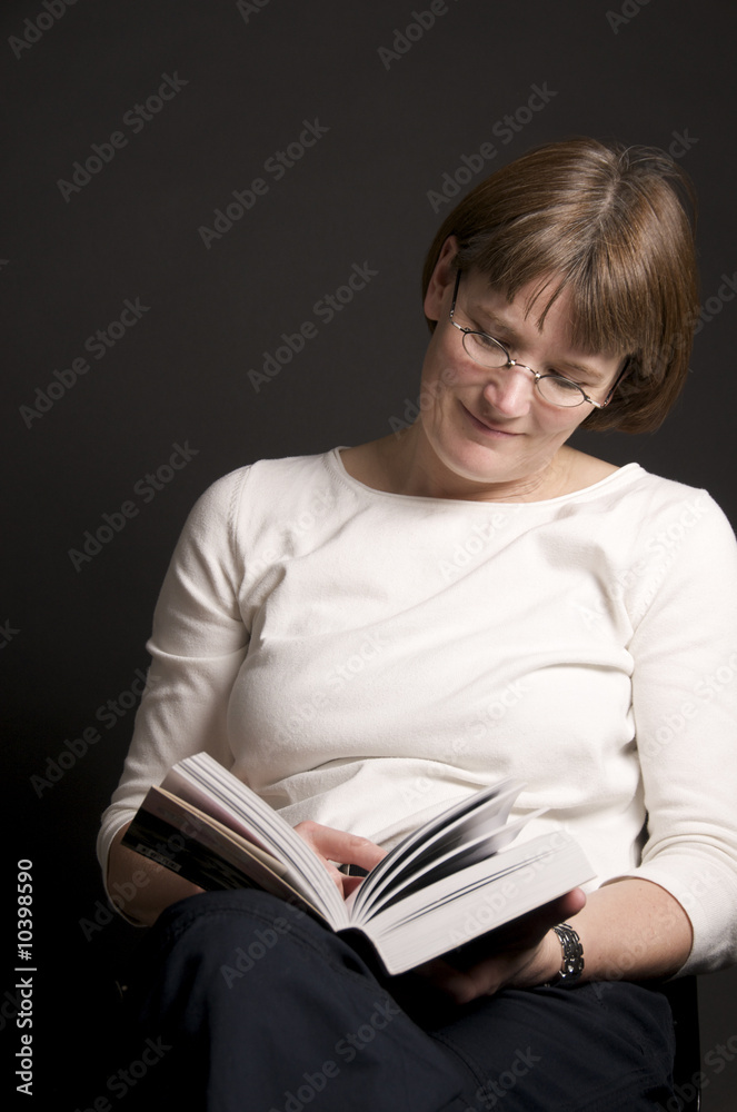 a middle-aged woman wiht glasses reading a book a middle-aged woman wiht glasses reading a book