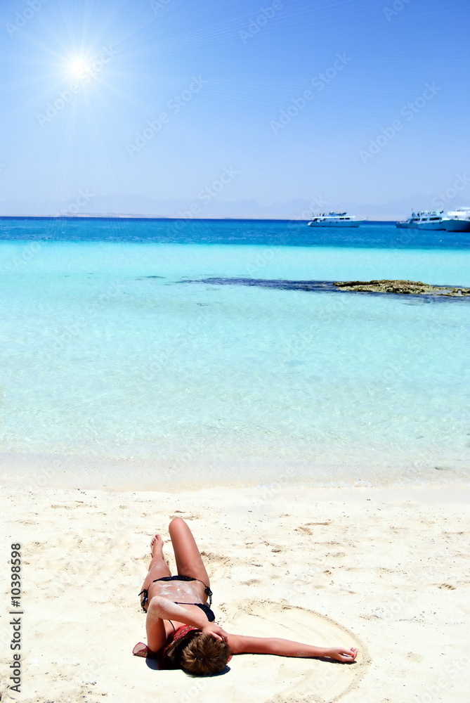 Young girl in bikini lying on white sand beach Young girl in bikini lying on white sand beach