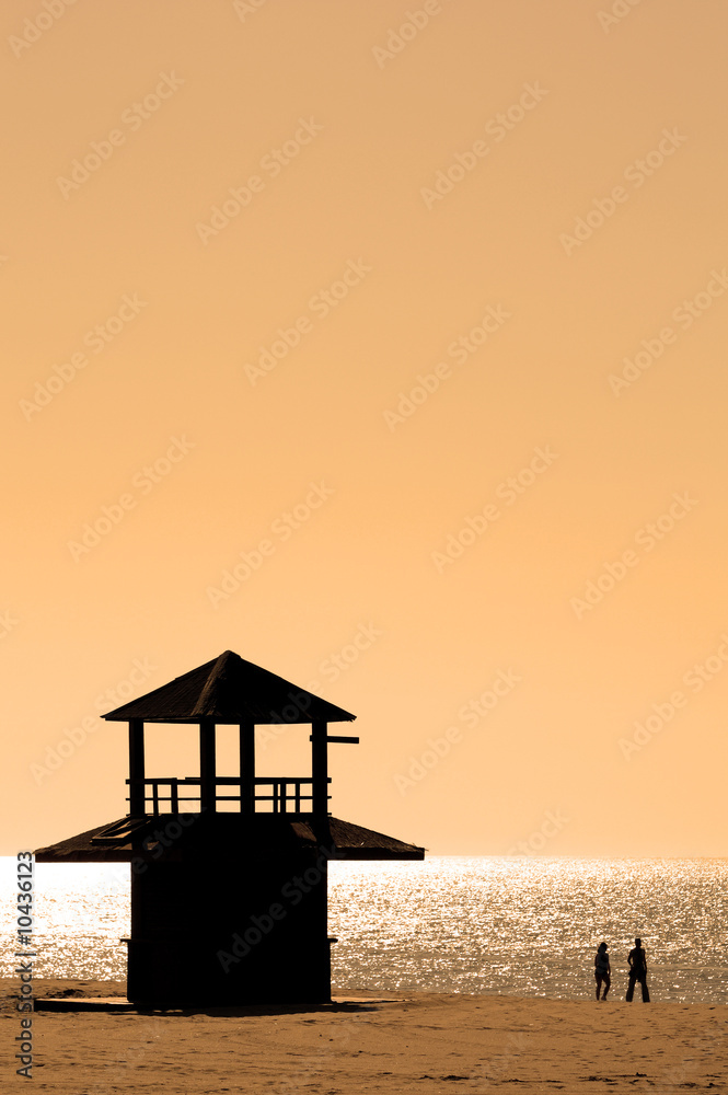 Couple in silhouette walking along sunny beach at sunset Couple in silhouette walking along sunny beach at sunset