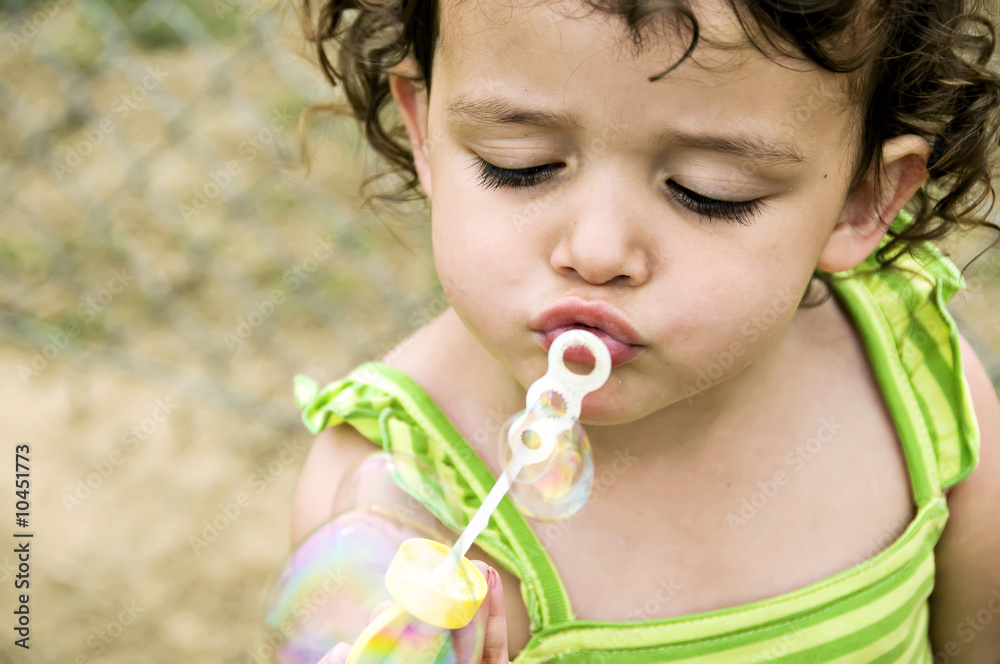 Beautiful little girl trying to blow bubbles.