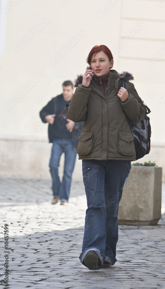 Redheaded girl student at the phone while is walking