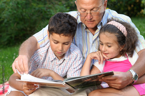 Grandfather,grandson and granddaughter reading a book