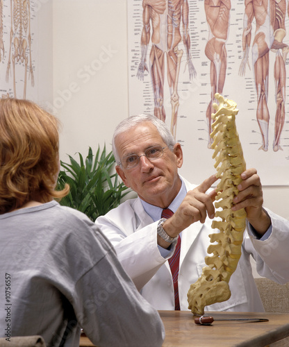 a chiropractor showing a patient a model of spine