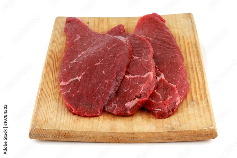 Three raw steaks on a wooden chopping board