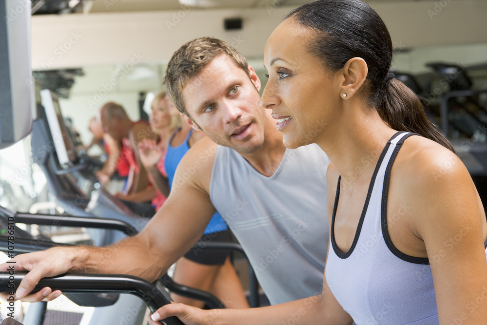 Personal Trainer Encouraging Woman Using Treadmill At Gym