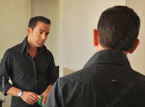 uomo con camicia scura ed orologio si guarda allo specchio photo