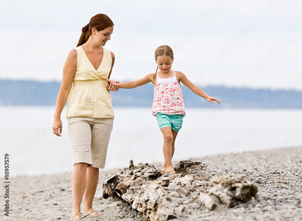 Mother helping daughter walk on log at beach Mother helping daughter walk on log at beach
