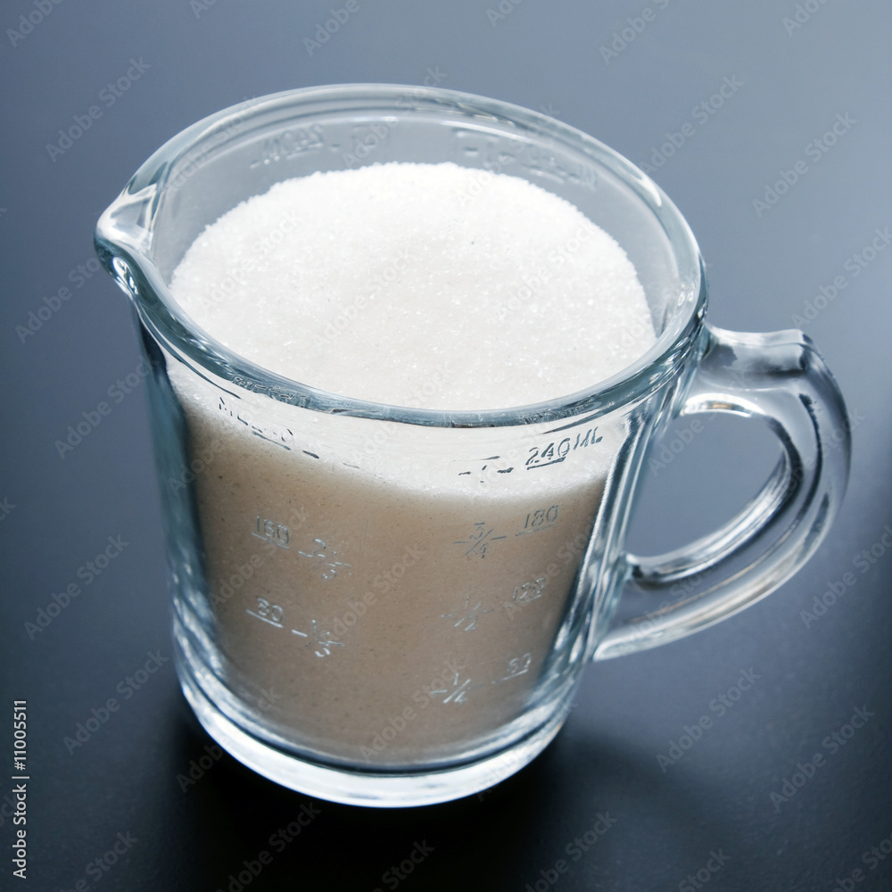 A glass measuring cup with sugar A glass measuring cup with sugar