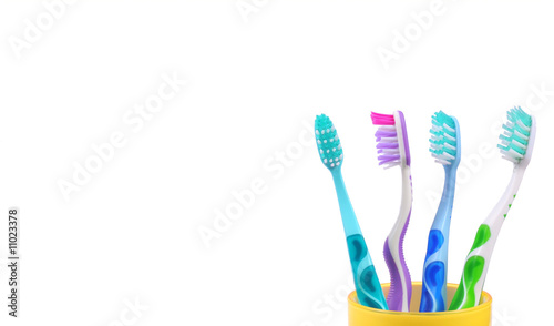 Four colorful toothbrushes in yellow mug isolated on white