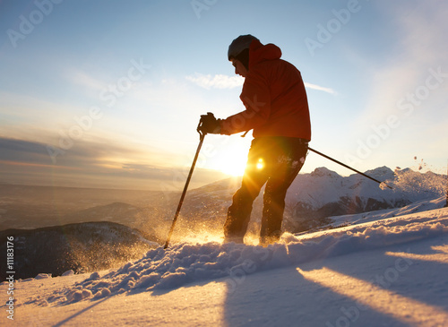 Freerider skier moving down in snow powder at sunset