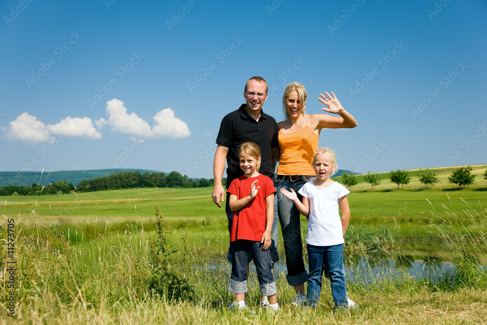 Familie auf der Wiese vor dem Teich winkt Familie auf der Wiese vor dem Teich winkt