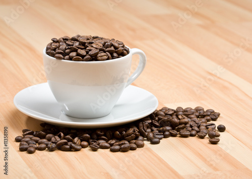 Cup with freshly roasted coffee beans on hardwood floor