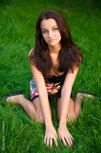 Beautiful young brunette sits on the green grass