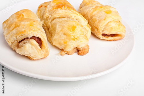 three sausage rolls on a white plate on a white background