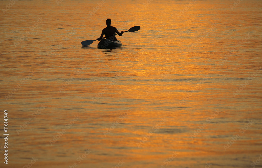 Silhouette of man kayaking at sunset
