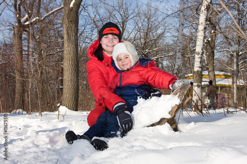 Mum with the son sit on snow in park