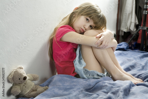 little sad girl sitting on the bed