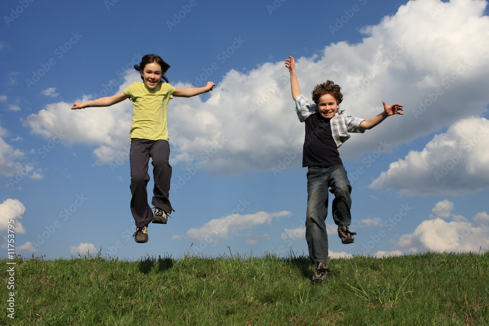 Kids running, jumping on green meadow against blue sky Kids running, jumping on green meadow against blue sky
