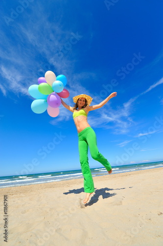 young woman with colorful balloons jumping on the beach © bereta