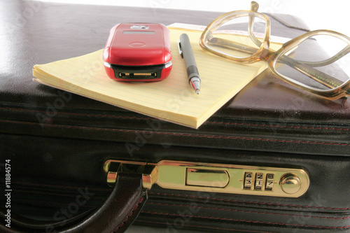 Briefcase with pad pen phone and glasses close up view