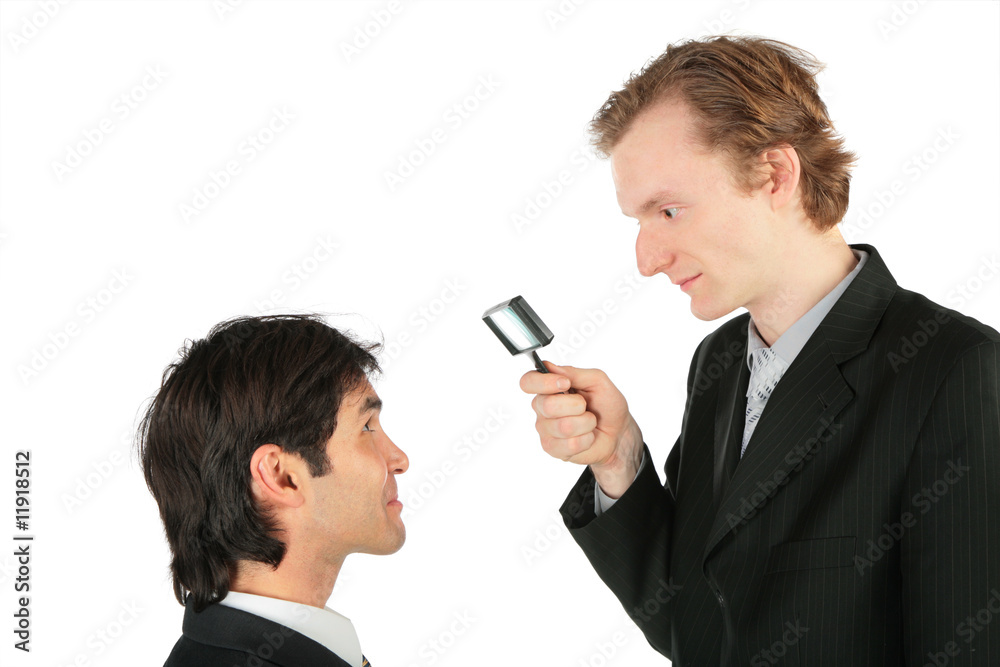 Naklejka premium One businessman looks at another through magnifying lens