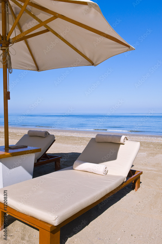 Deck chairs on the beach under an umbrella.