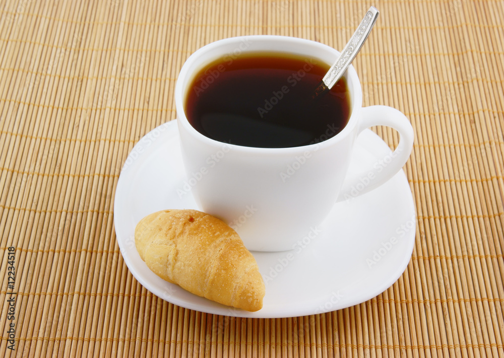 Small croissant and white cup of coffee with teaspoon Small croissant and white cup of coffee with teaspoon
