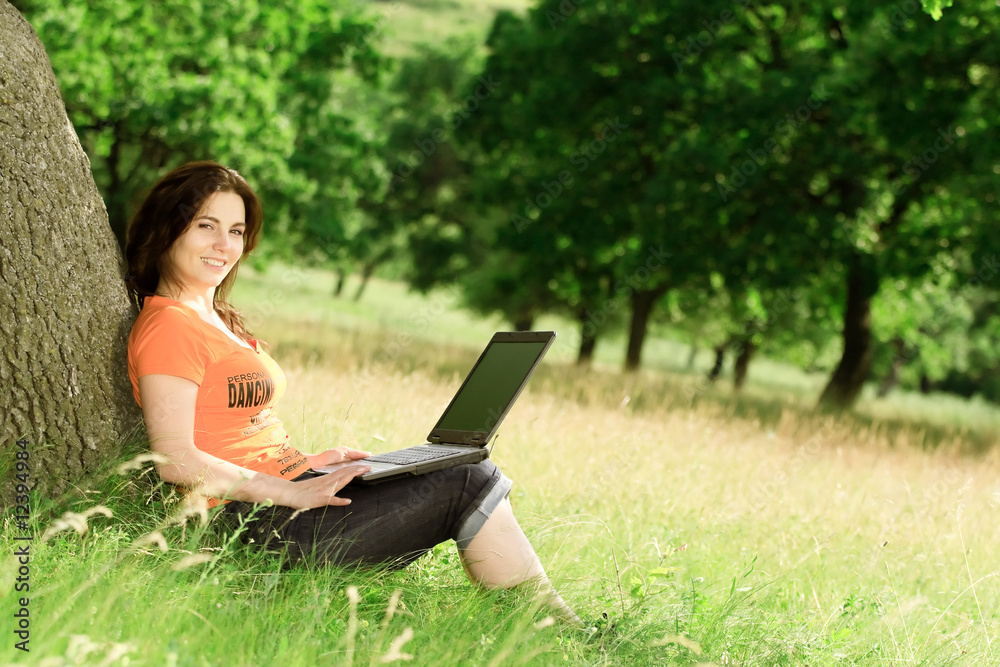 girl sitting in a meadow and working with her laptop computer