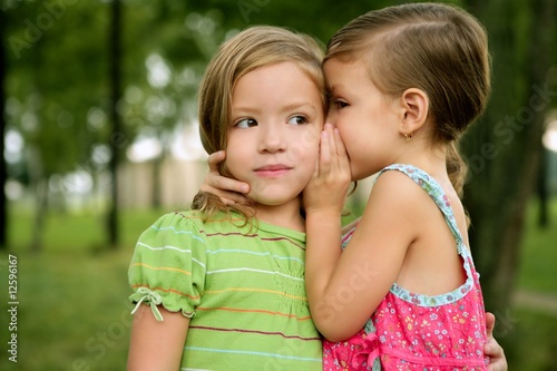 Two twin little sister girls whisper in ear photo