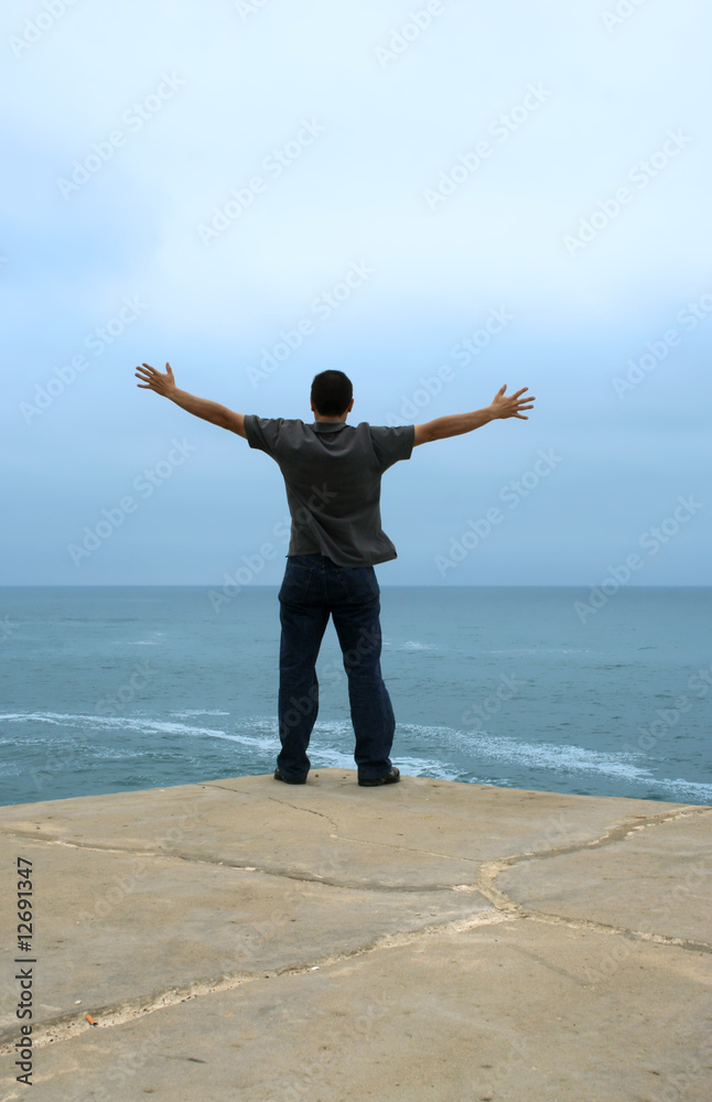 young man with arms open contemplating the ocean young man with arms open contemplating the ocean