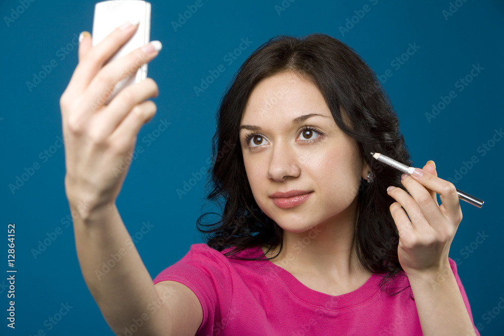 Woman applying eyeliner in compact mirror Woman applying eyeliner in compact mirror