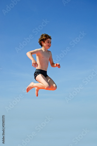 Fototapeta Naklejka Na Ścianę i Meble -  Boy jumping against blue sky