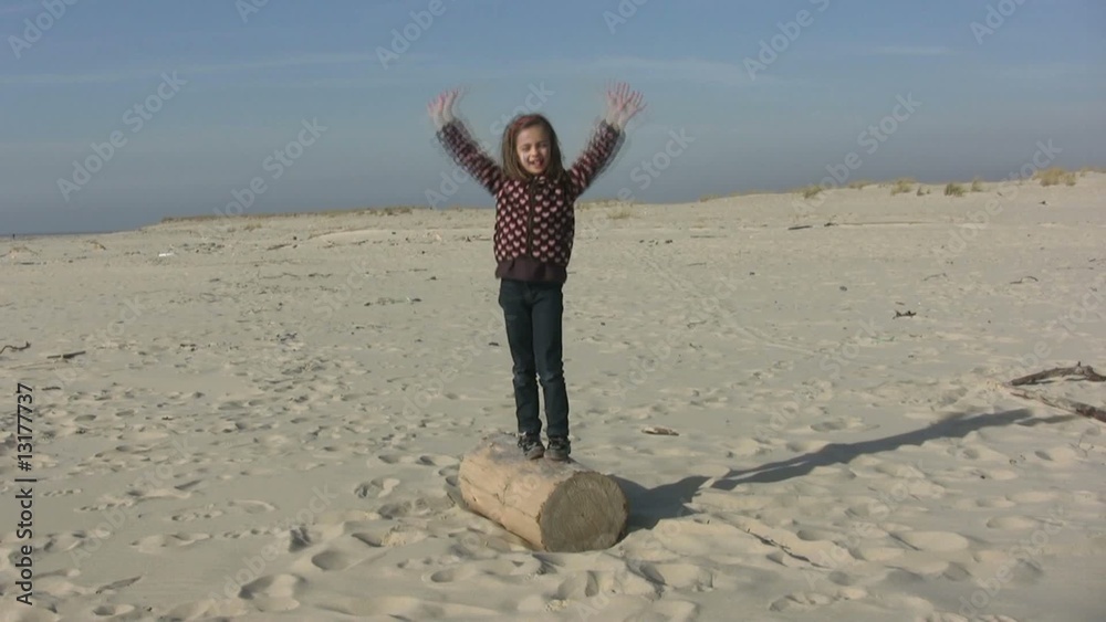 fillette dansant sur un tronc d'arbre sur la plage