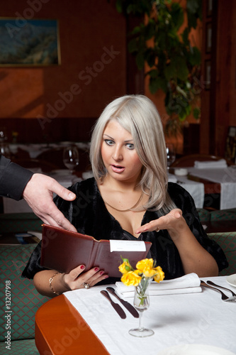 Blond girl in a restaurant show a huge bill for food