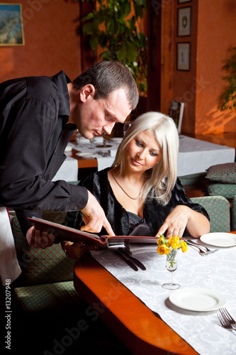 The waiter helped visitor with a choice of eating in a restauran