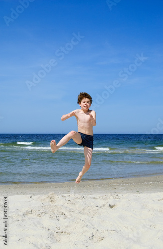 Boy jumping on beach against blue sky