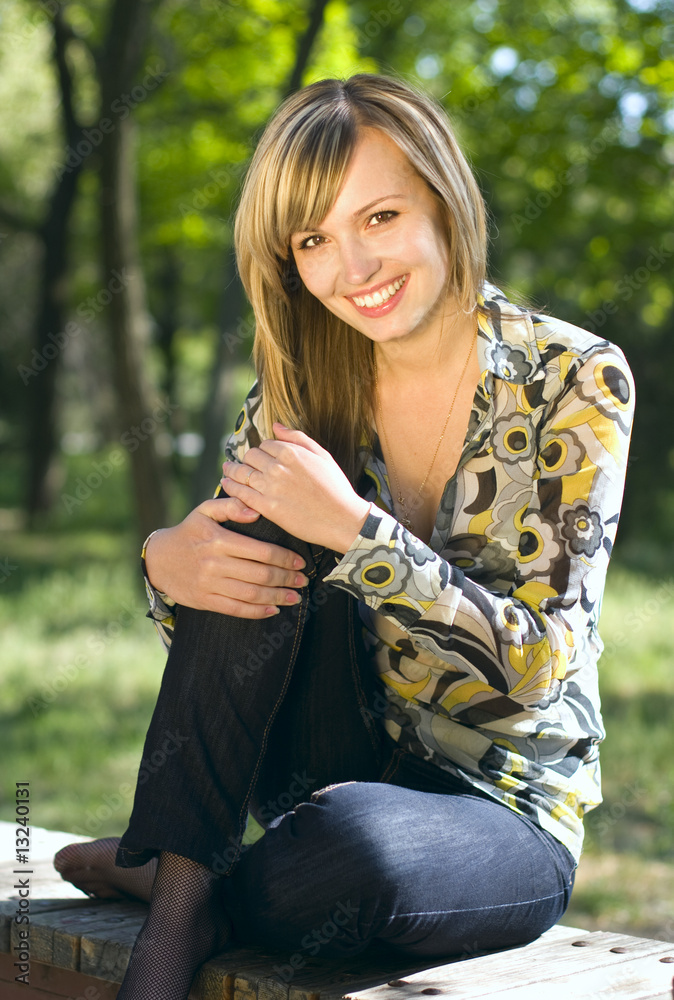 A young blond girl sitting in a park and smiling A young blond girl sitting in a park and smiling