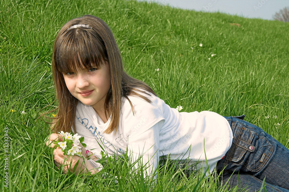 Fototapeta premium Mädchen liegt im Gras mit Blumen in der Hand