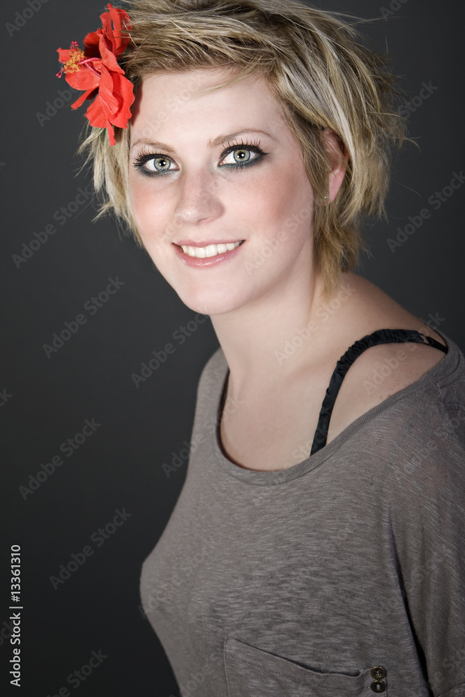 Naklejka premium Shot of a Smiling Blonde Girl with Red Flower in her Hair