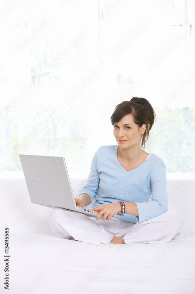 Young woman is on couch and working on laptop