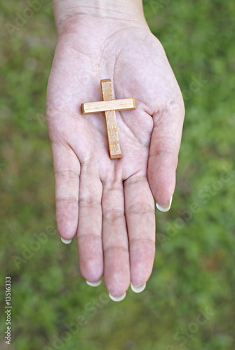 Wooden cross in female hand with green grass background