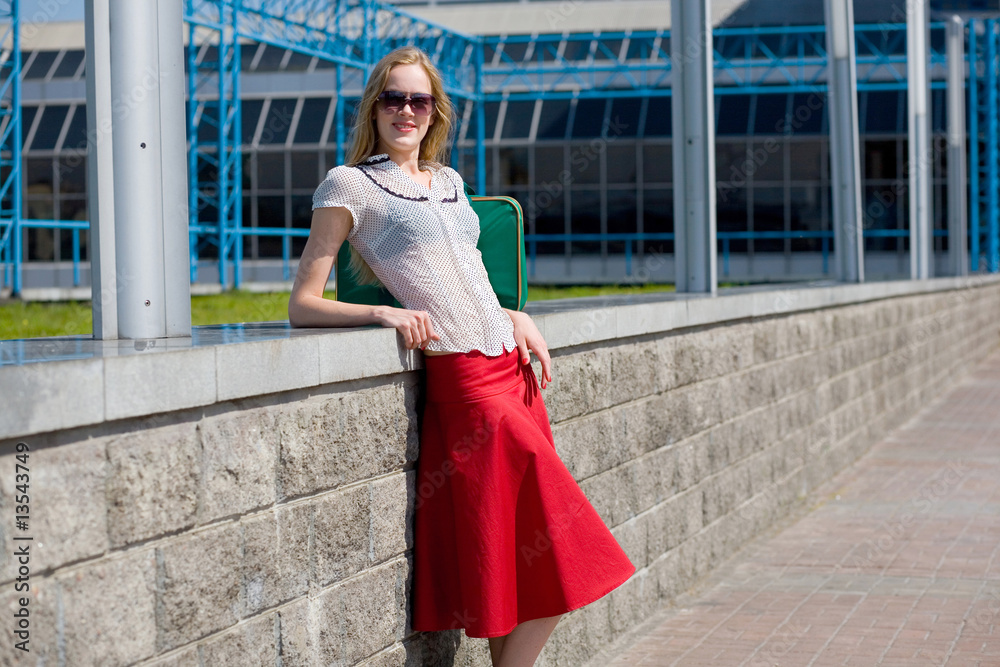 Fototapeta premium Smiling sexy blonde girl wearing red skirt. Near green bag.