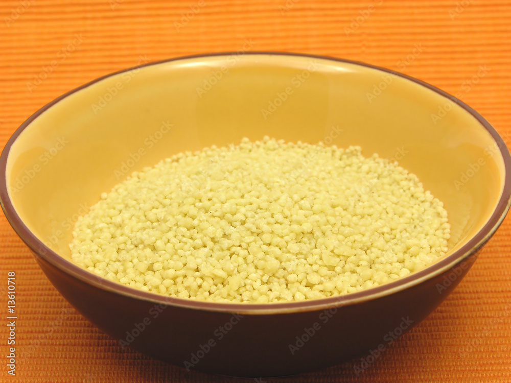 Couscous in einer orangen Keramikschale auf orangem Hintergrund Couscous in einer orangen Keramikschale auf orangem Hintergrund