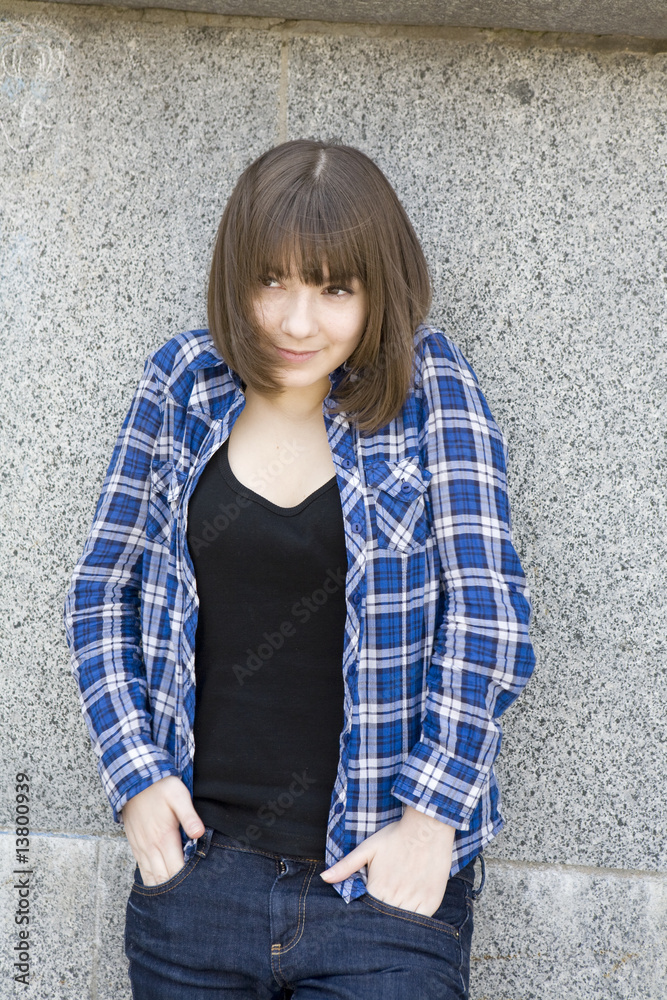 teen girl in chequered shirt standing at stone wall teen girl in chequered shirt standing at stone wall