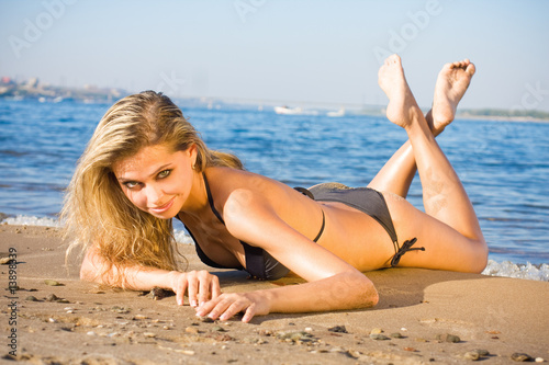 Outdoor portrait of a sexy young girl in black bikini lying on t